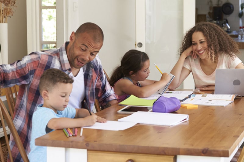Top 5 Benefits of Installing a Geothermal System. Photo of a family of four working on homework together at the kitchen table.